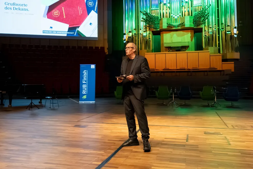 Dekan Prof. Dr. Michael Kellmann hält die Grußworte bei RUB Finish 2026 auf der Bühne des Audimax der RUB