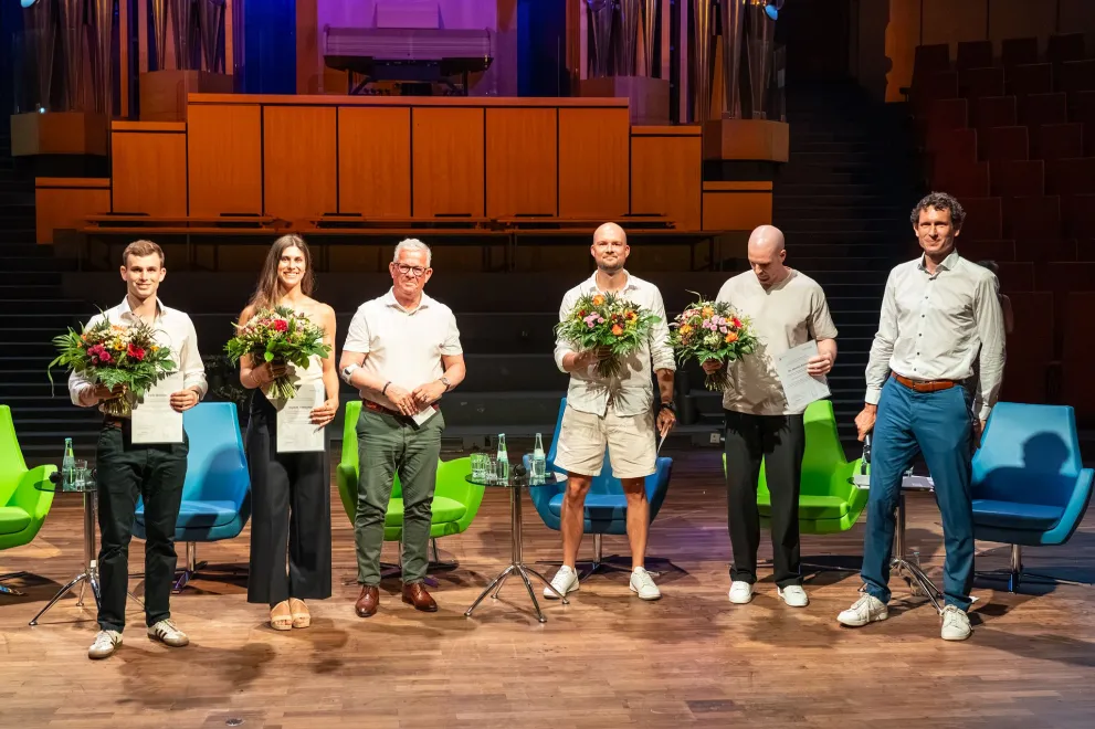 Geehrte mit Blumensträußen auf der Bühne bei der Abschlussfeier RUB Finish 2026 im Audimax der RUB